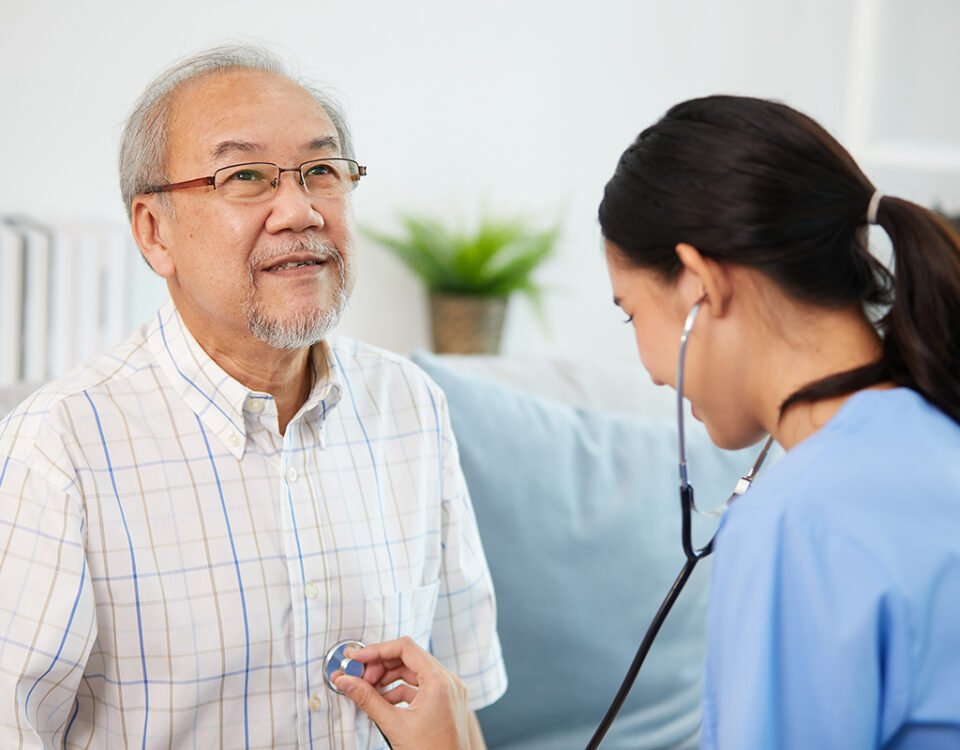 nurse or caregiver using stethoscope to examine senior man at home